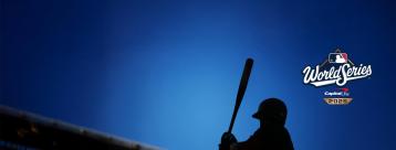 Silhouette of a baseball player raising a bat against a dusk-blue sky in a stadium, with the WORLD SERIES™ presented by Capital One logo in view.