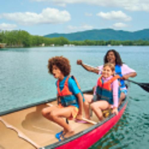 Dos niños y un adulto se ríen mientras navegan en canoa por un lago. 