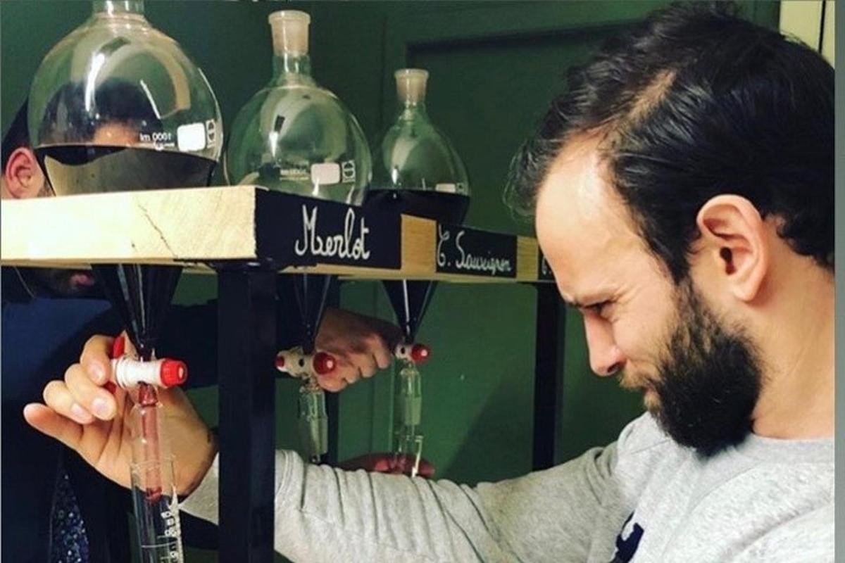 a man cutting a bottle of wine in front of wine bottles