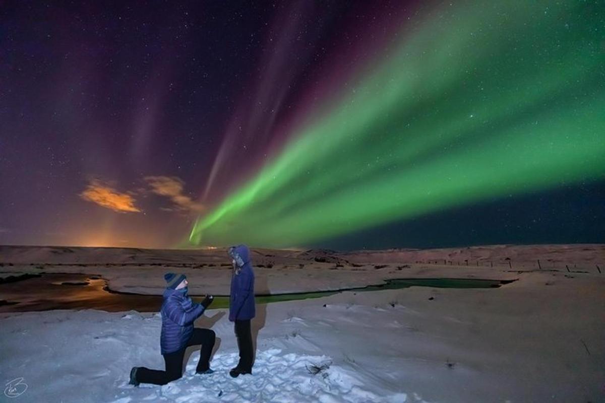 duas pessoas em pé na neve observando a aurora boreal
