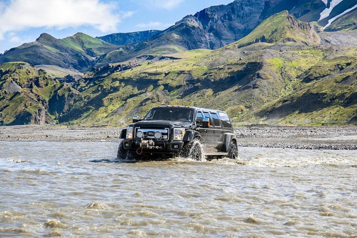 Un camión circulando por un río con montañas al fondo.