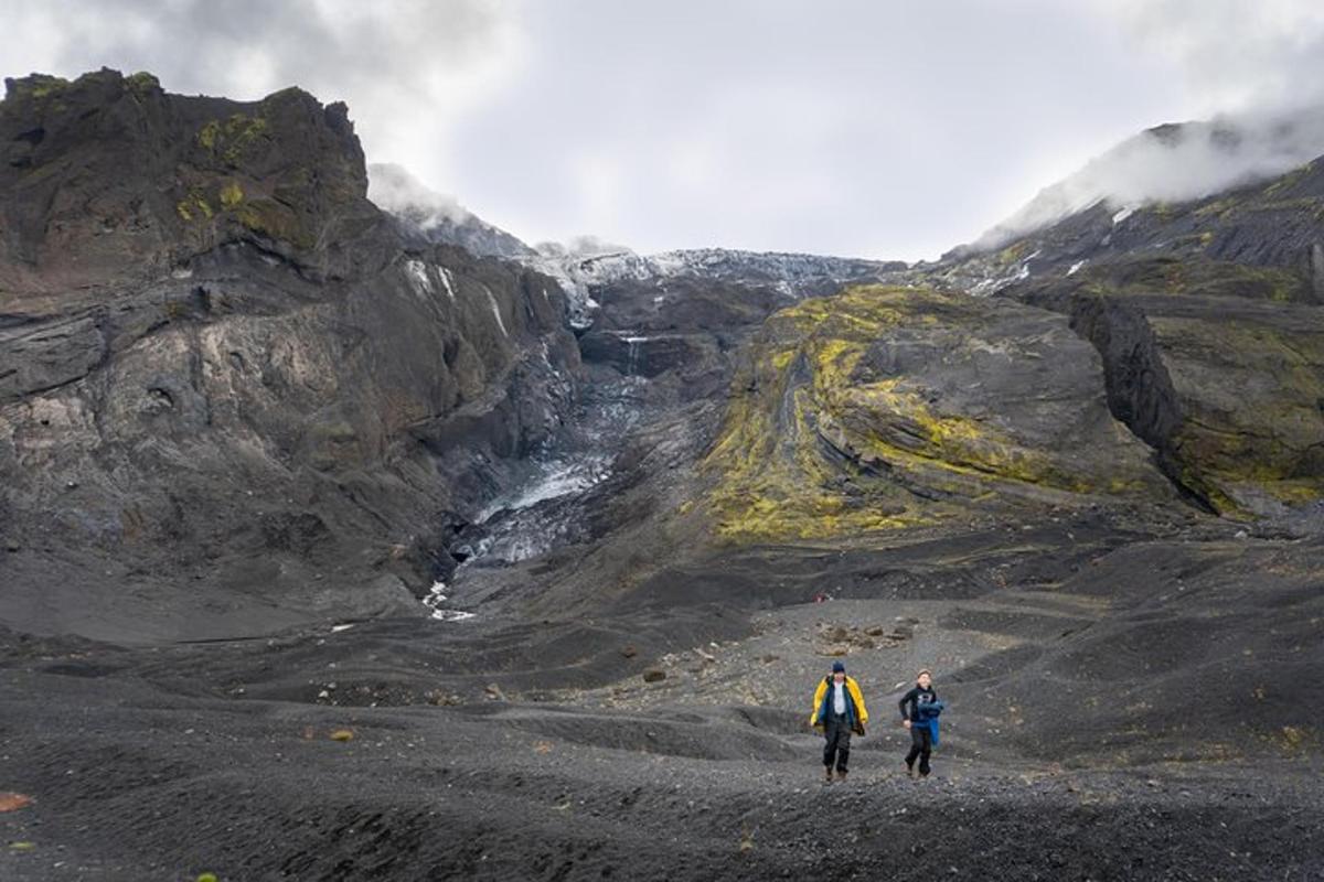 Dos personas caminando por una montaña rocosa con una cascada.