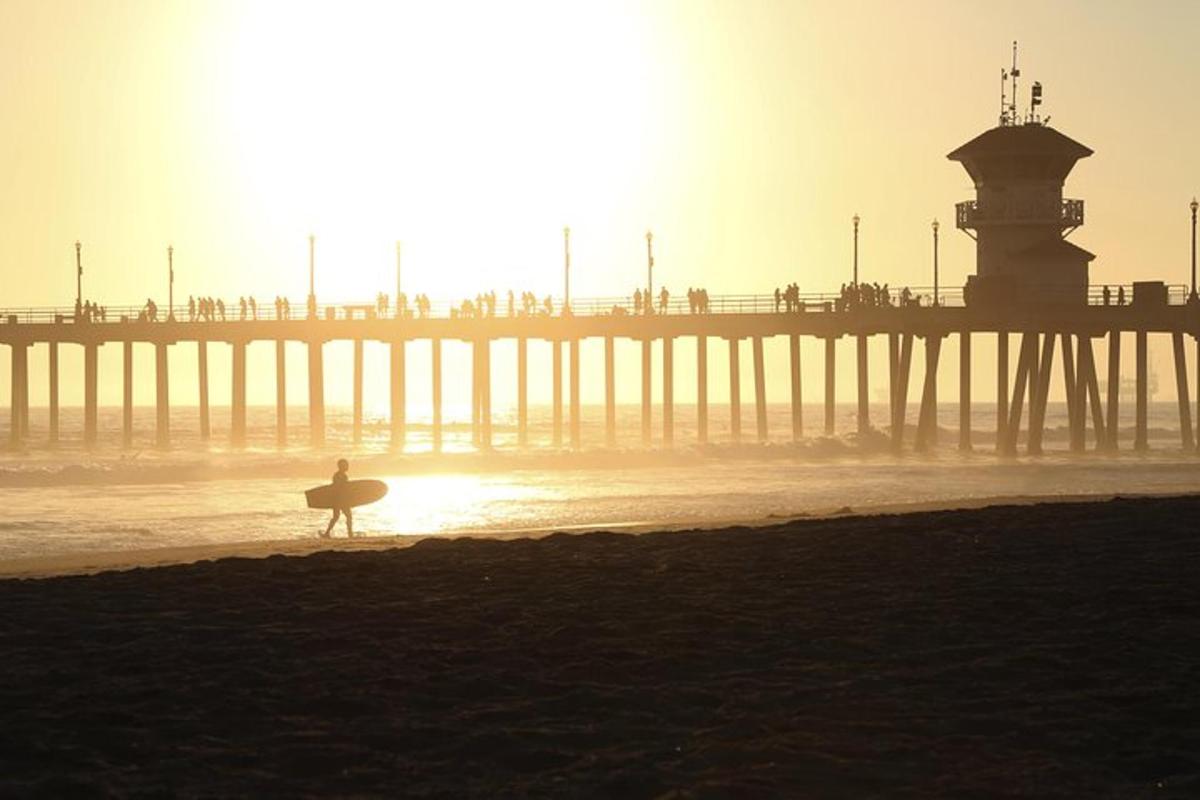 a person walking on the beach with a surfboard in front of a pier