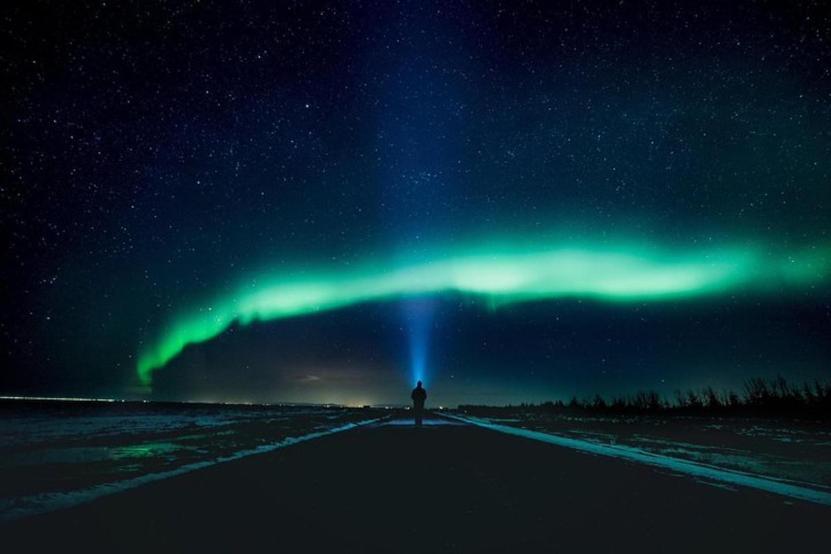 Una persona parada en una carretera bajo la aurora boreal.