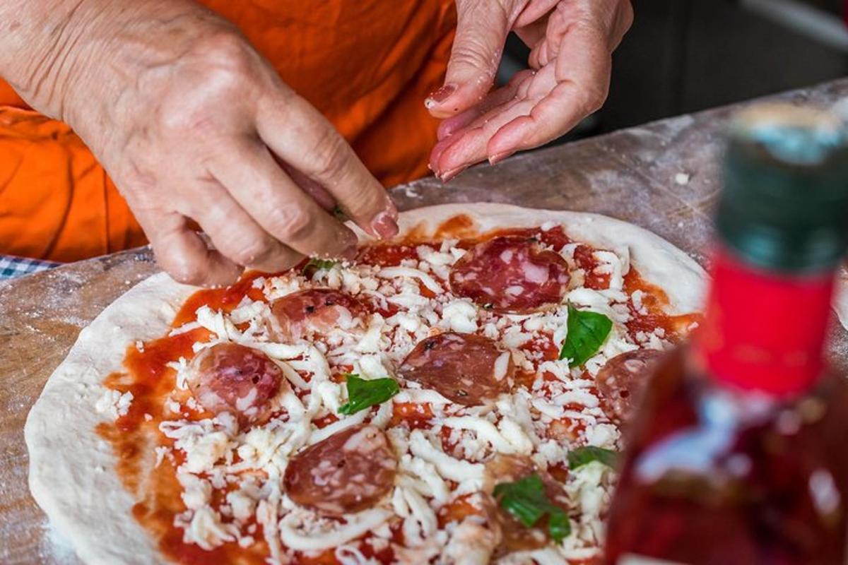một người phủ pepperoni và phô mai lên trên bánh pizza