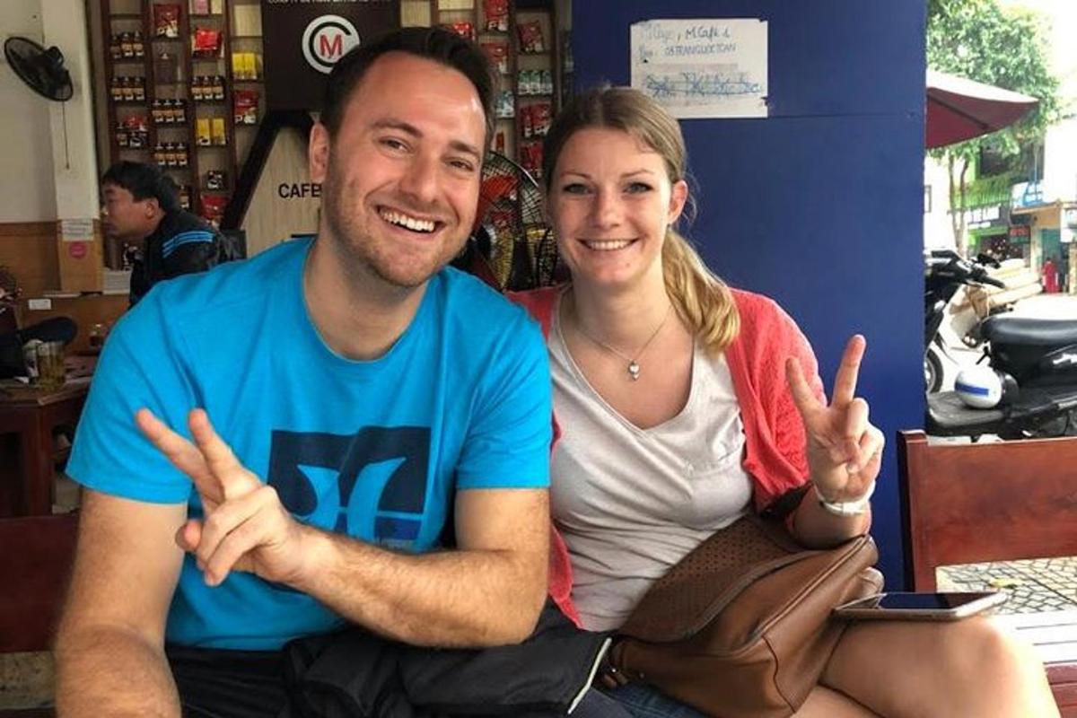 um homem e uma mulher sentados em um banco fazendo o sinal da paz