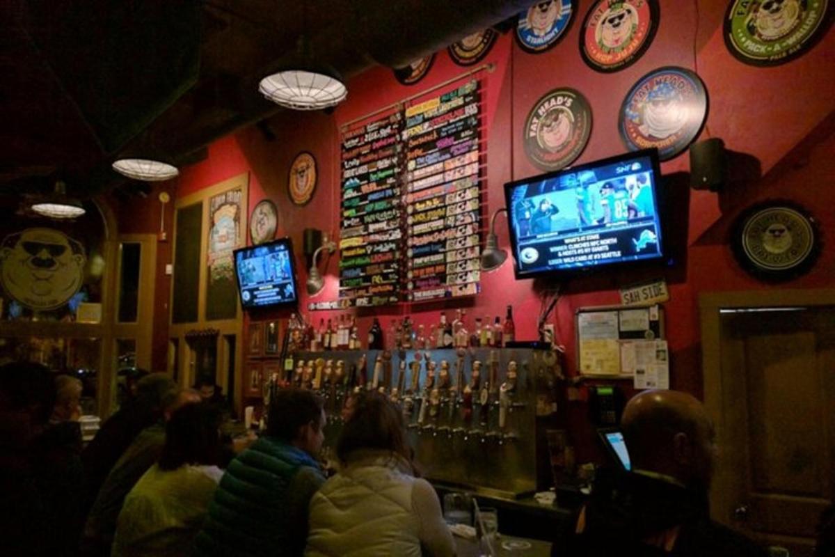 a group of people sitting at a bar with televisions