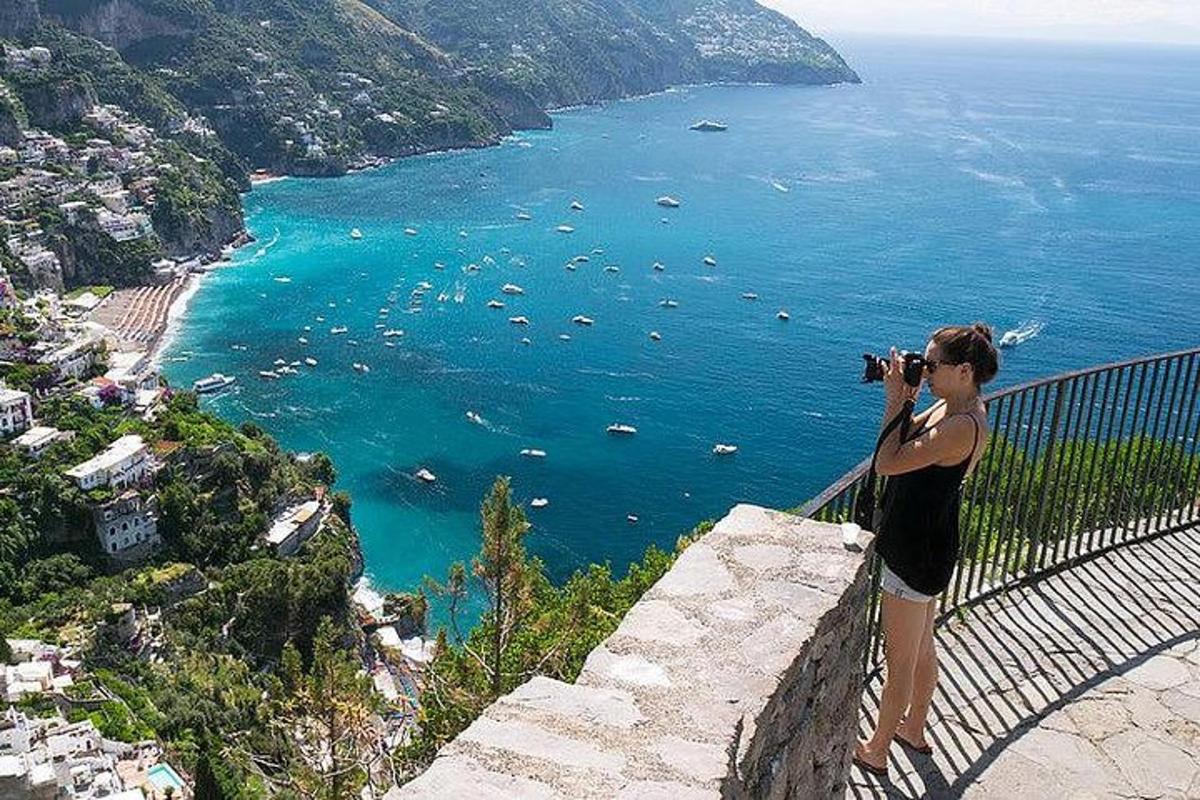 Una mujer parada en un muro tomando una fotografía del océano.