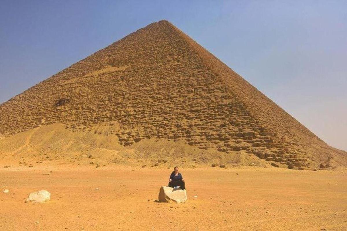 una persona seduta su una roccia di fronte a una piramide