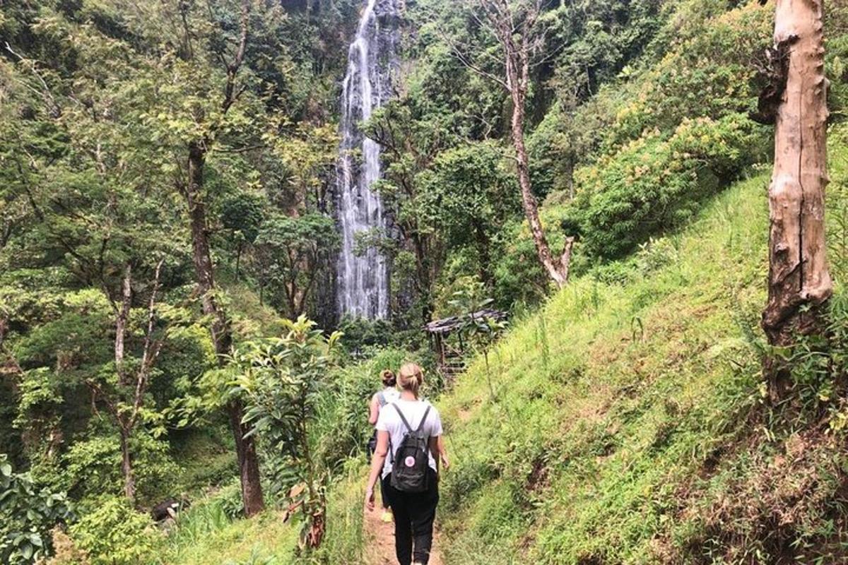 dua orang berjalan menyusuri denai di hadapan air terjun