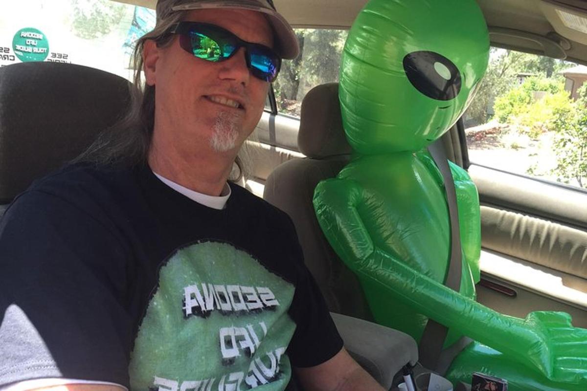 un uomo seduto in macchina accanto a una mascotte verde