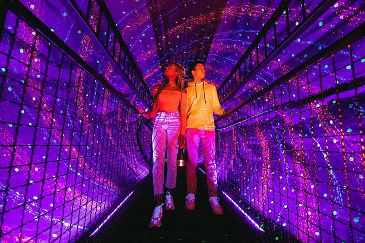 two people walking through a tunnel with purple lights
