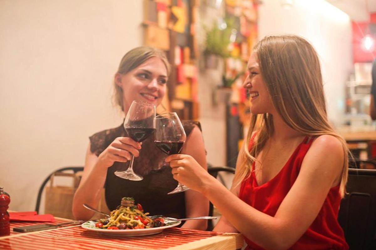 duas mulheres sentadas à mesa com taças de vinho