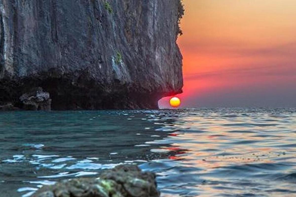 um pôr do sol sobre o oceano com uma grande rocha