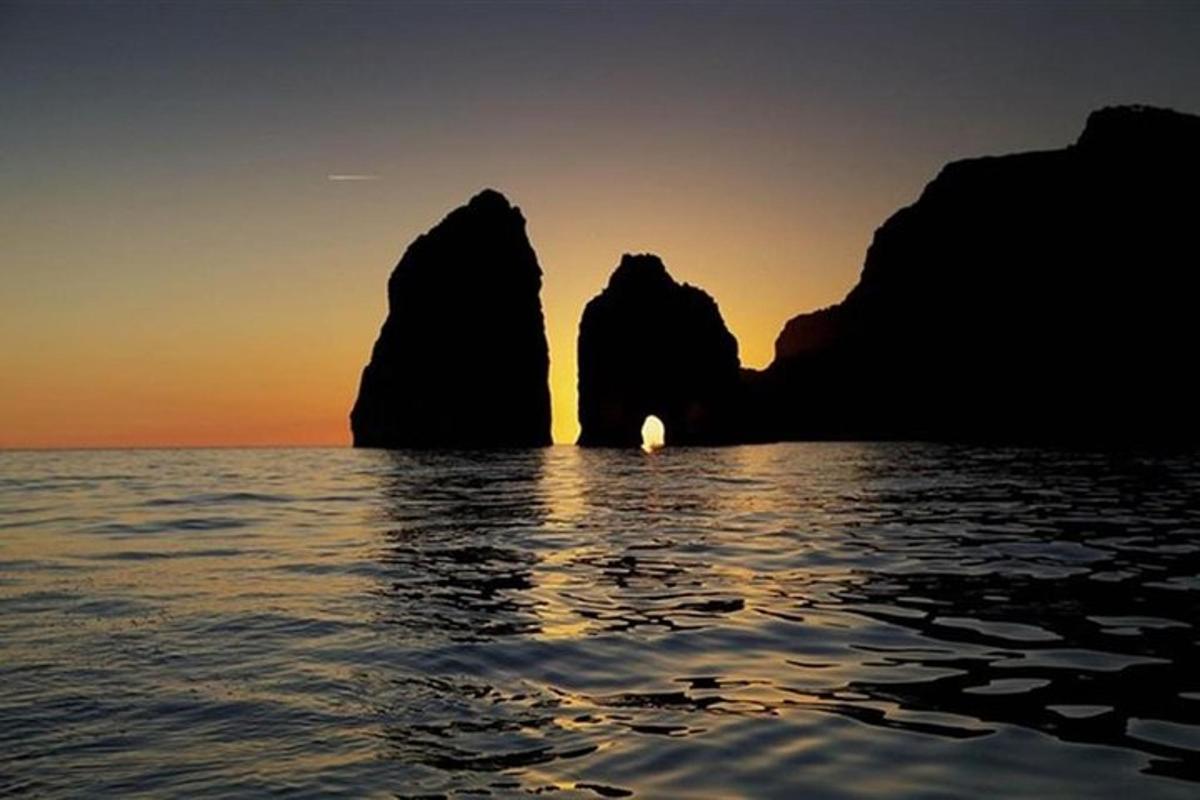 a sunset over the ocean with rocks in the water