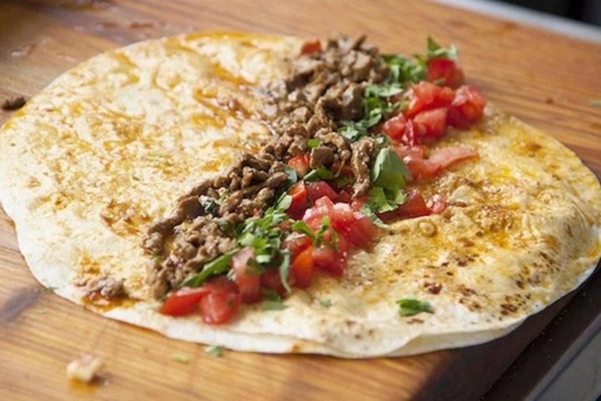 a pizza with meat and tomatoes on a wooden table