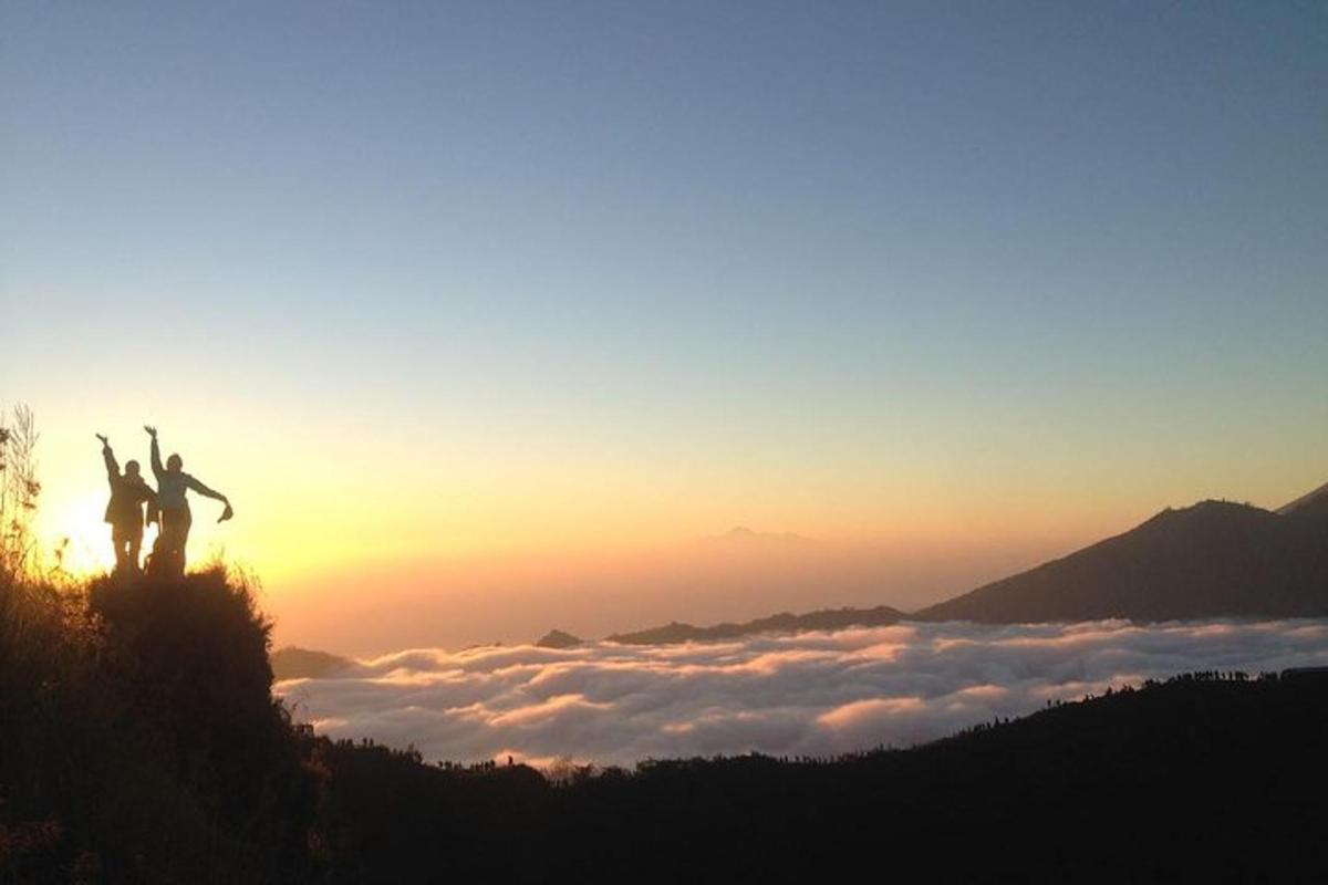 two people standing on top of a mountain at sunset