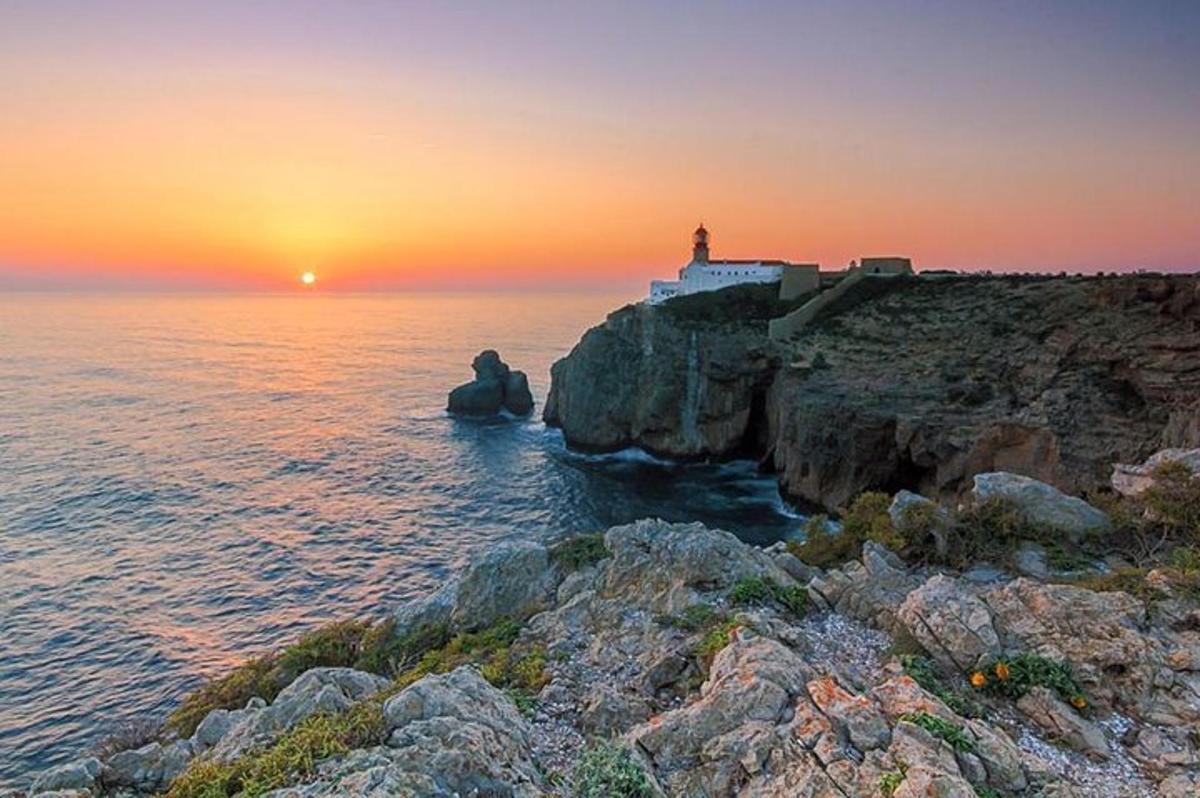 a lighthouse on a cliff near the ocean at sunset