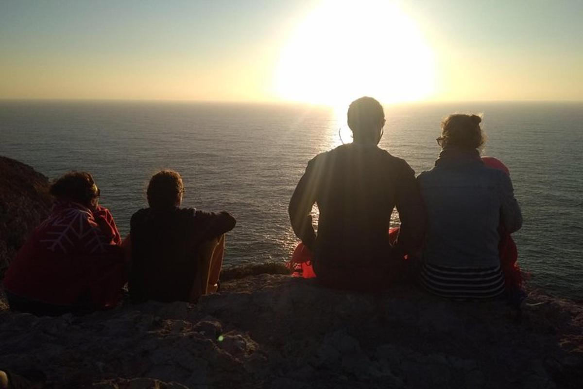 a group of people sitting on a cliff looking at the ocean