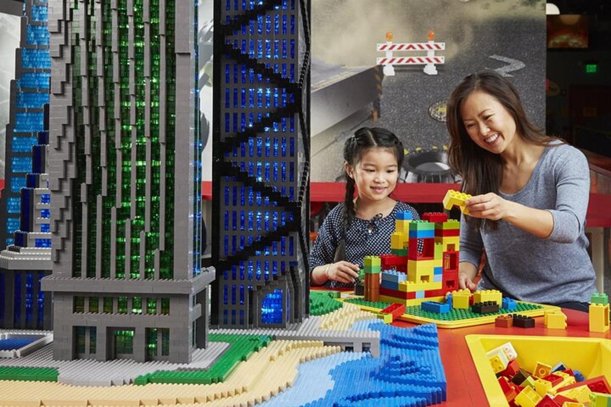 a woman and child playing with a lego model of a city