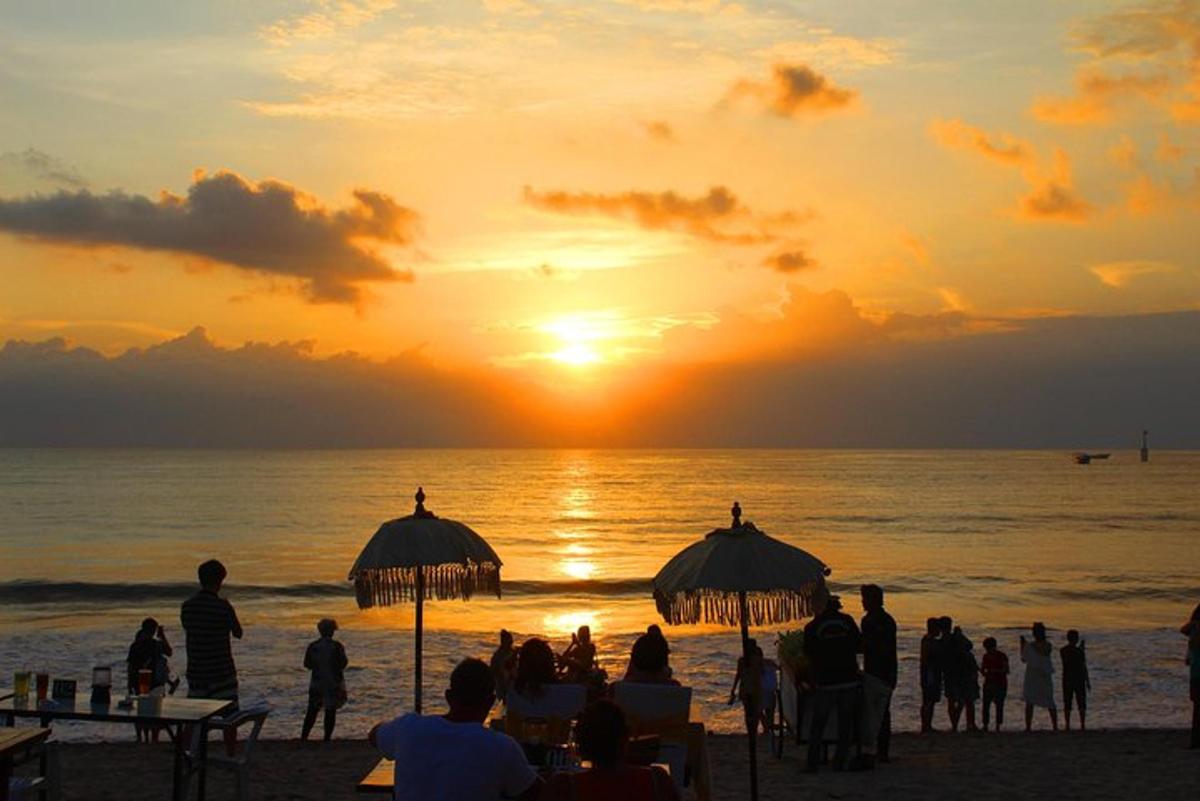 sekumpulan orang berdiri di pantai melihat matahari terbenam
