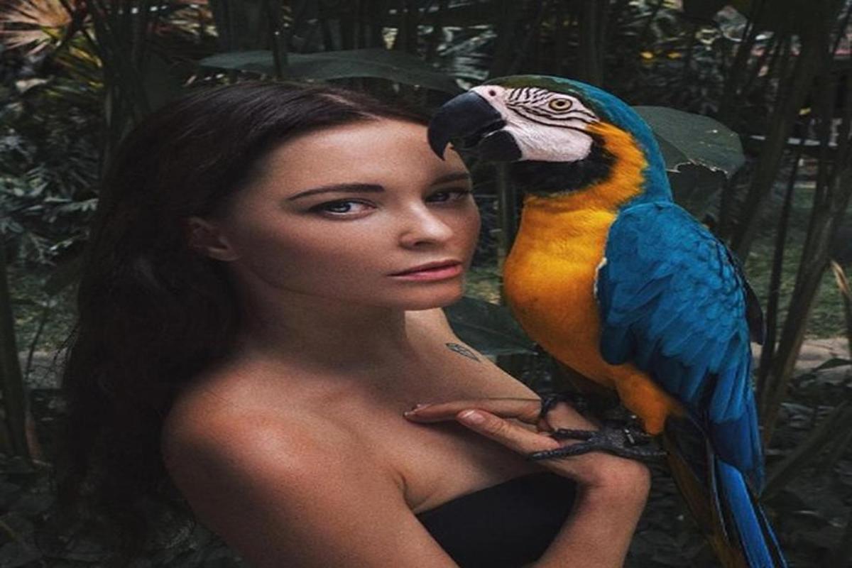 žena držící na rameni barevného papouška
