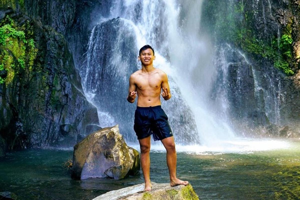 seorang lelaki berdiri di atas batu di hadapan air terjun