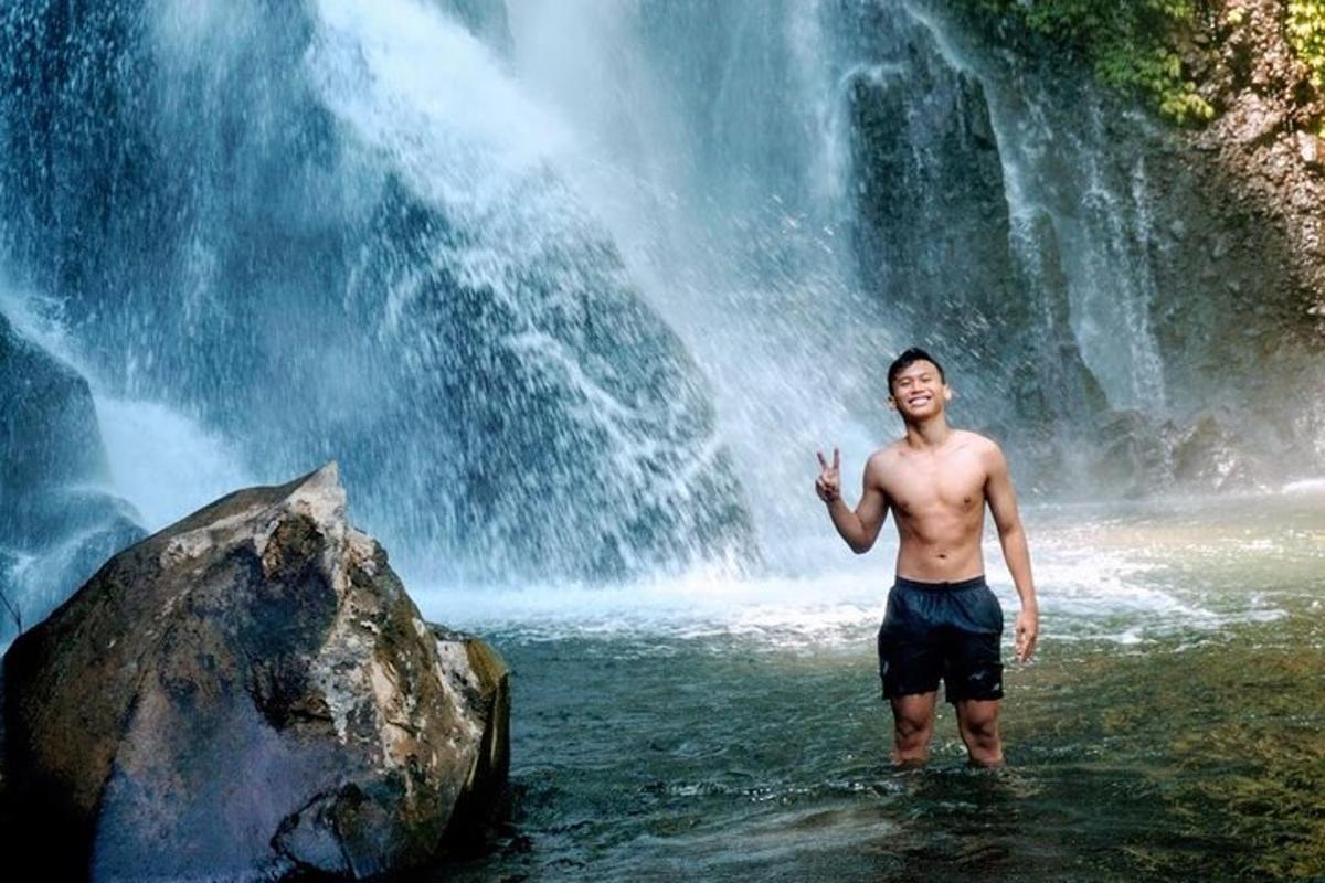 seorang lelaki berdiri di dalam air di hadapan air terjun