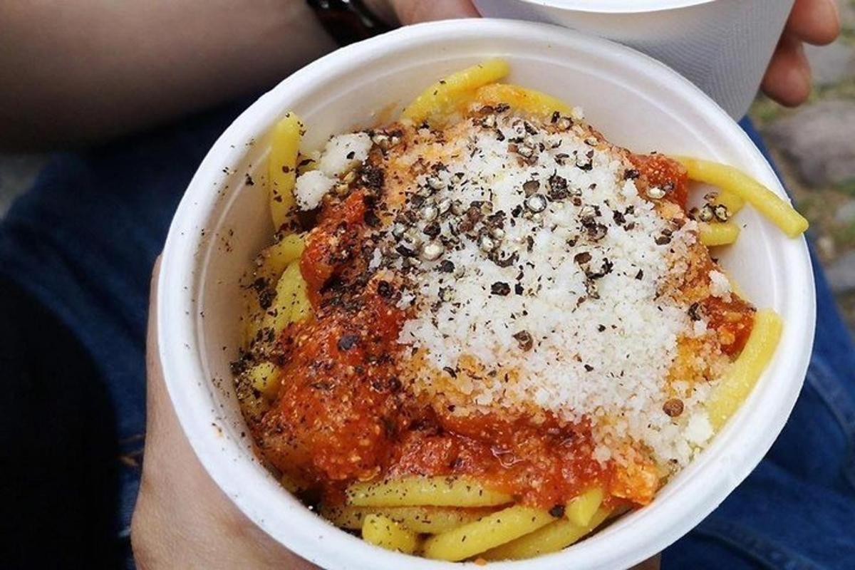 a person holding a bowl of pasta with sauce
