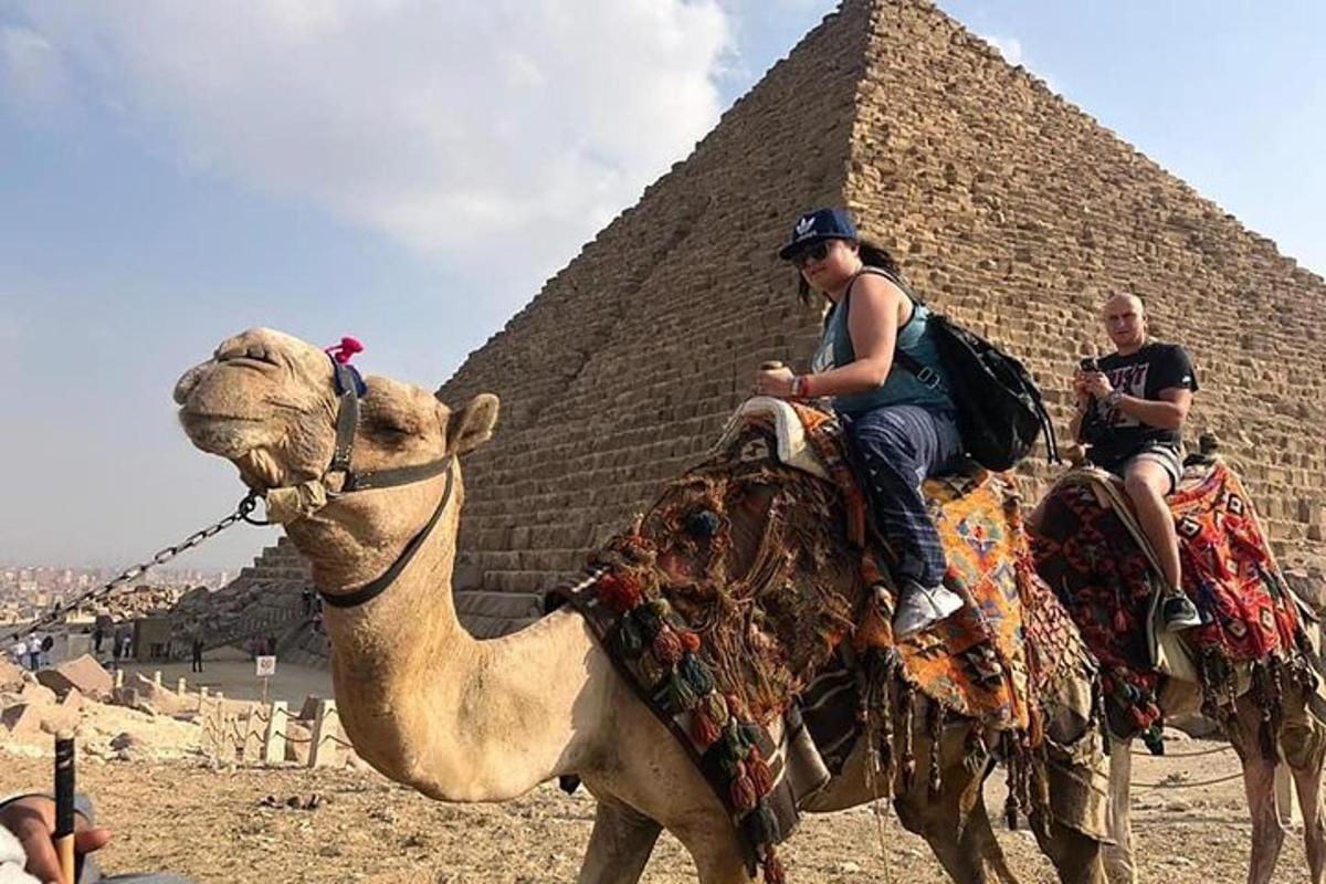 two people riding on a camel in front of a pyramid