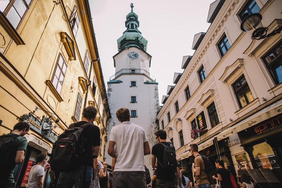 skupina lidí jdoucích po ulici s hodinovou věží