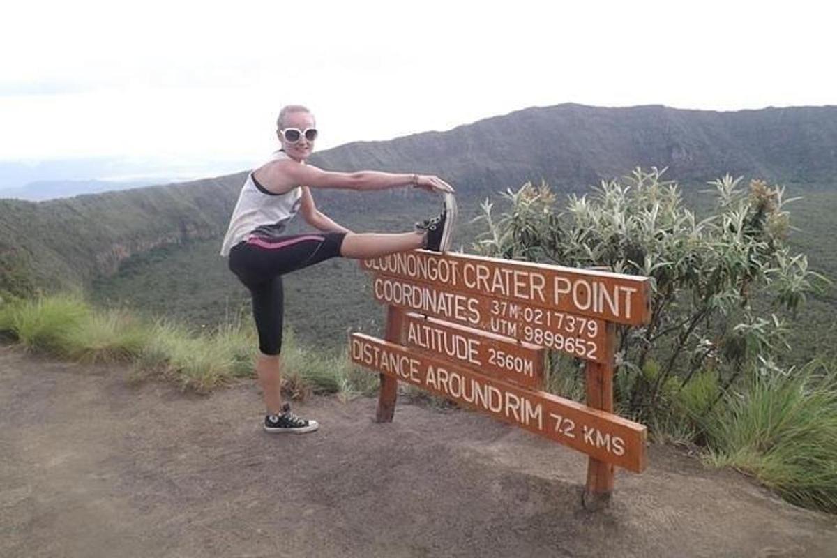 Una mujer parada sobre un cartel en la cima de una montaña.
