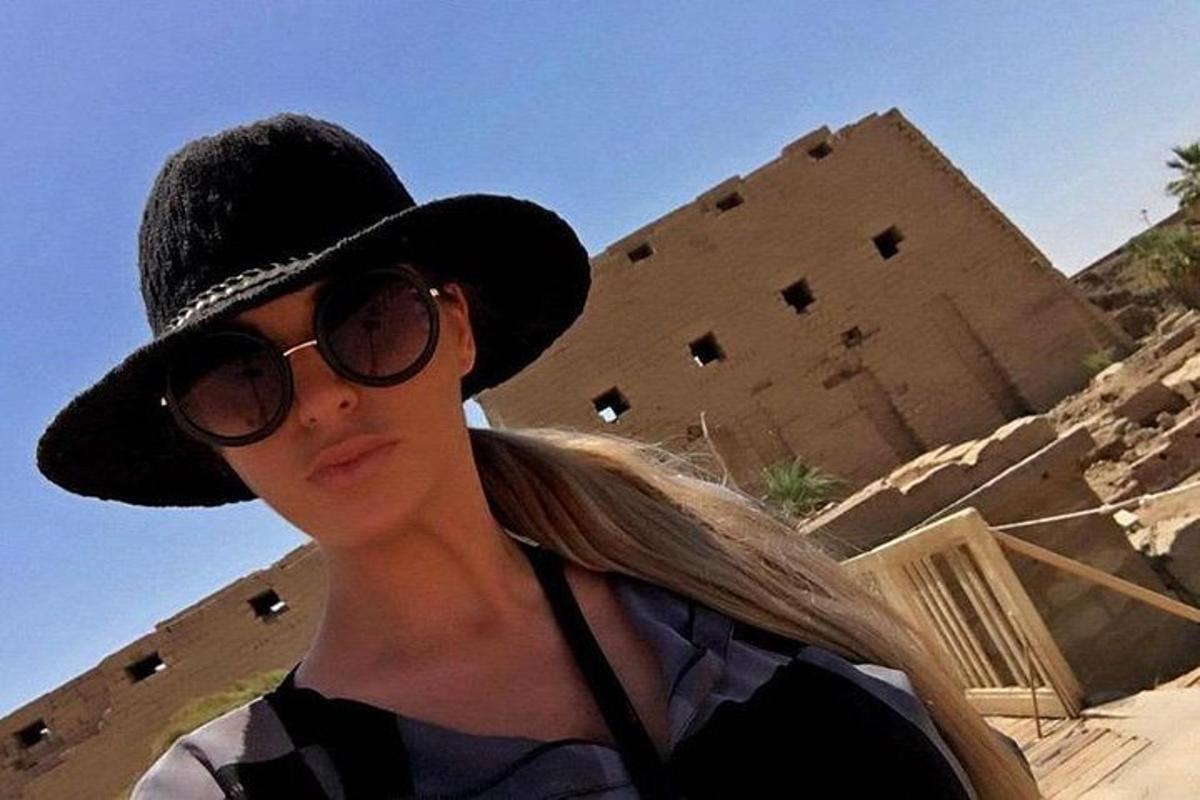 Una mujer con sombrero y gafas de sol frente a un edificio.