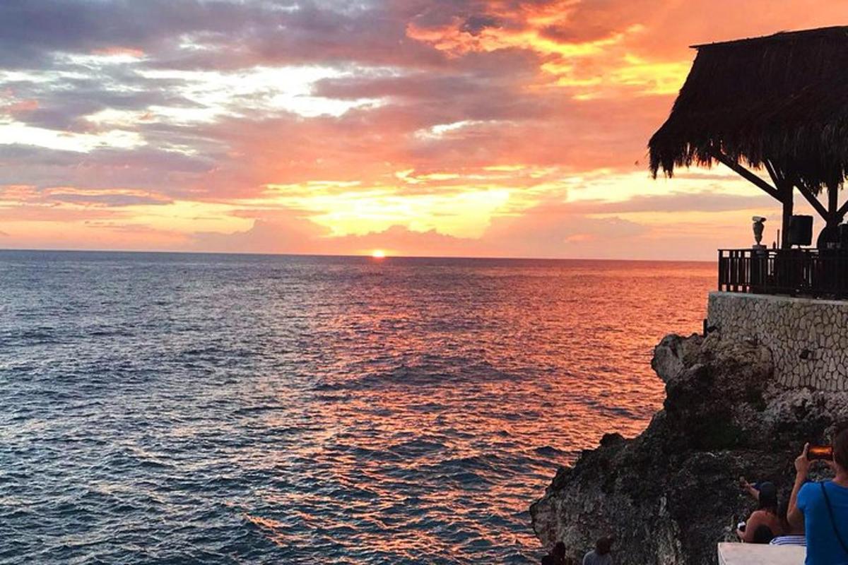 Západ slunce nad oceánem s lidmi stojícími na útesu