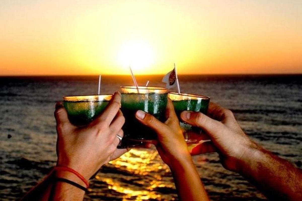 due persone che tengono in mano dei drink di fronte all'oceano