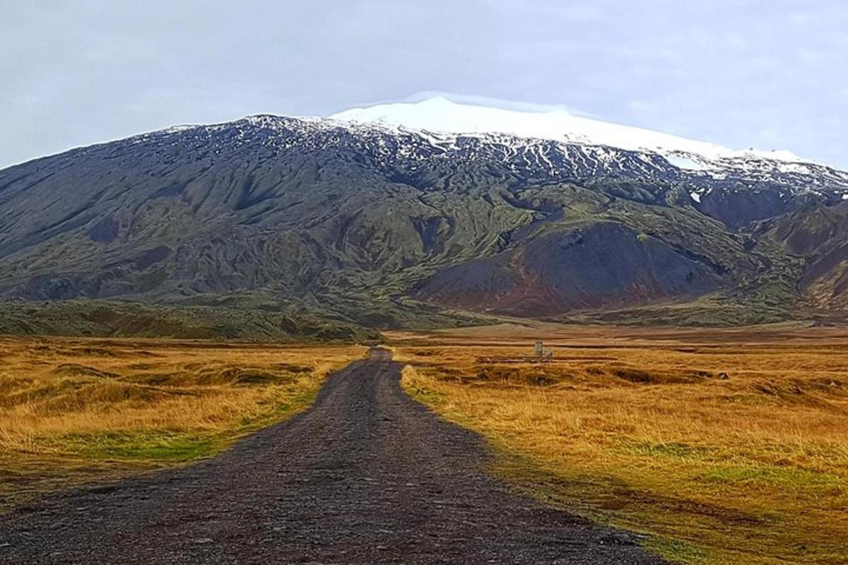 a dirt road in front of a snow covered mountain