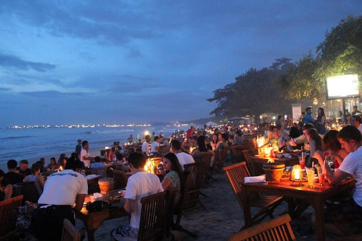 Una multitud de personas sentadas en mesas en la playa por la noche.