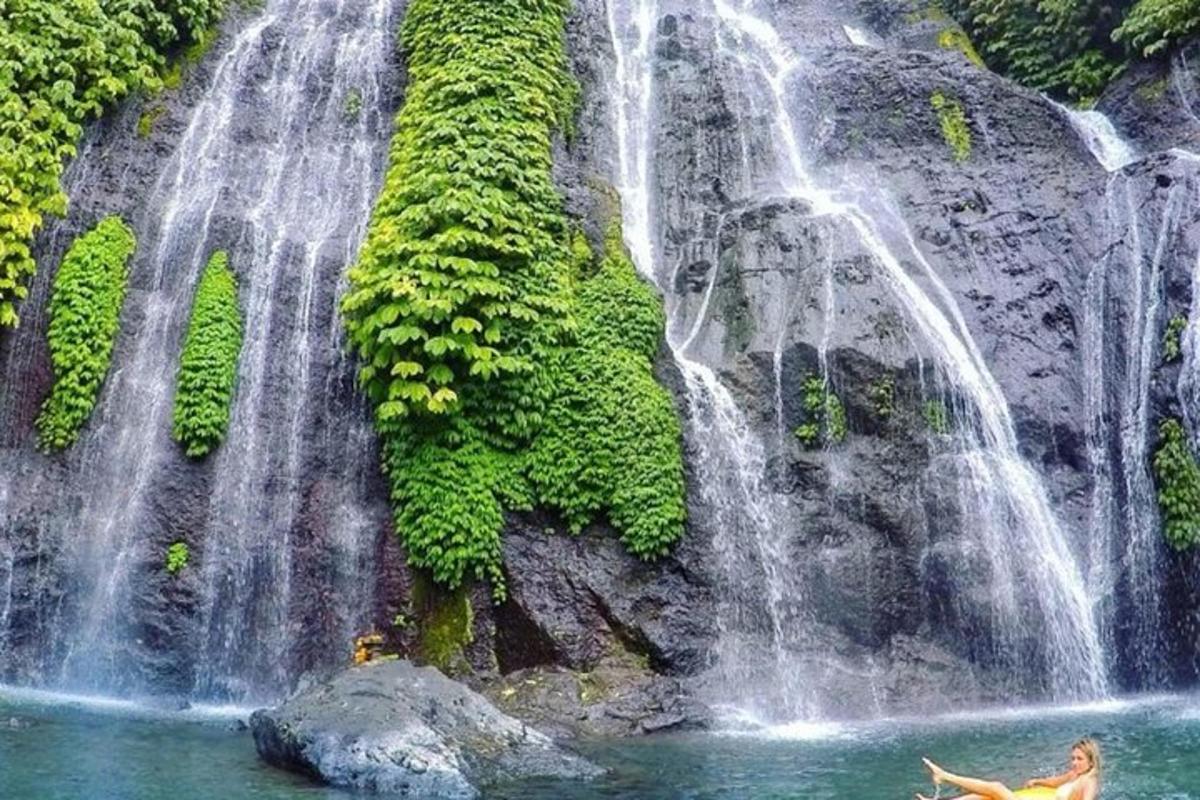 a waterfall with people swimming in the water in front of it