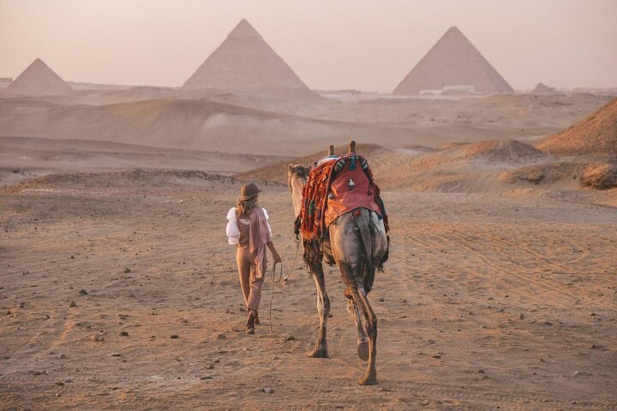 una donna che cammina su un cammello nel deserto con le piramidi sullo sfondo