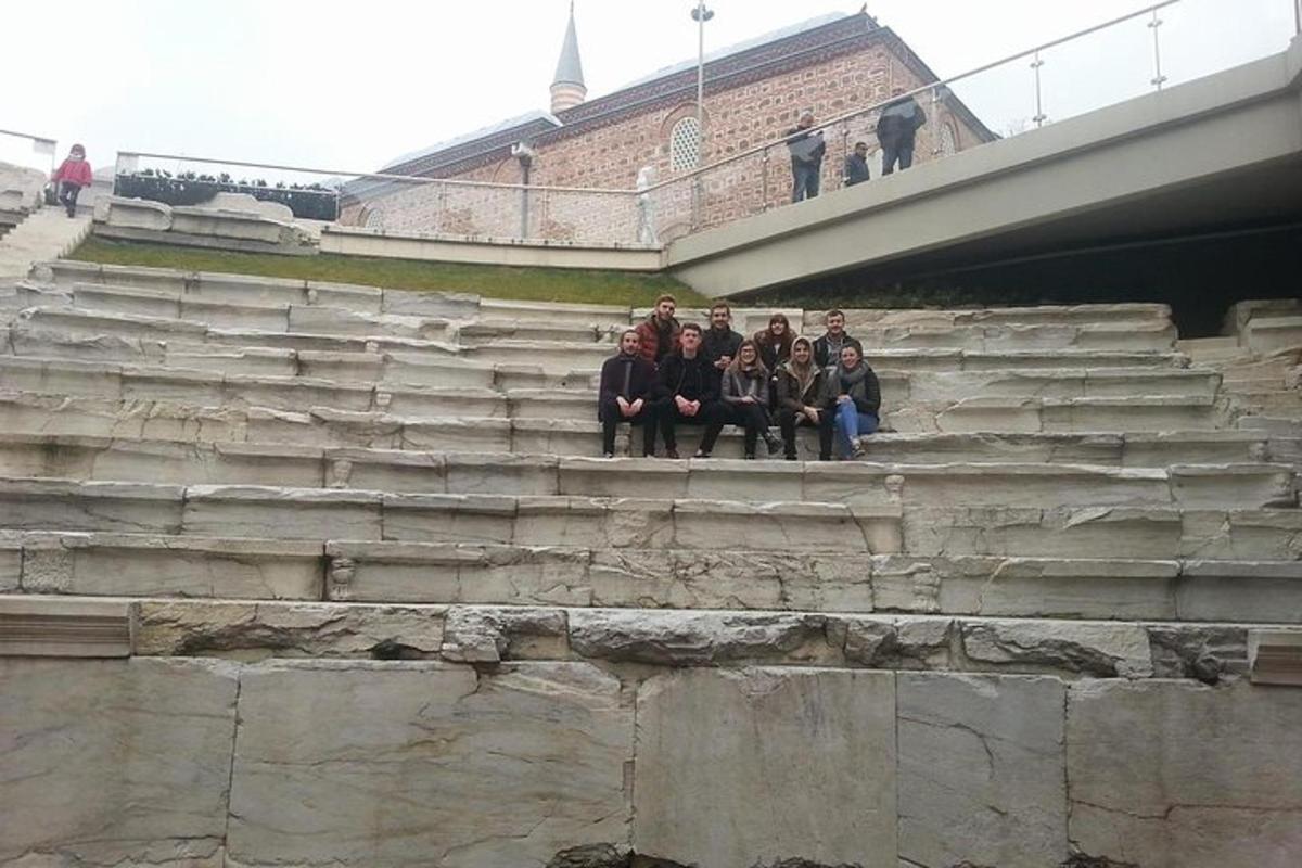 skupina lidí sedících na schodech pod mostem