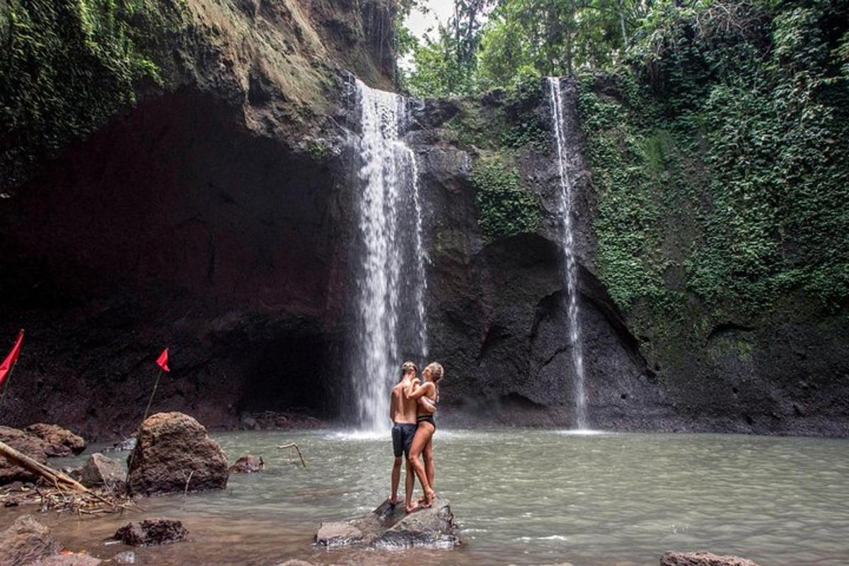 Dos personas paradas en el agua frente a una cascada.