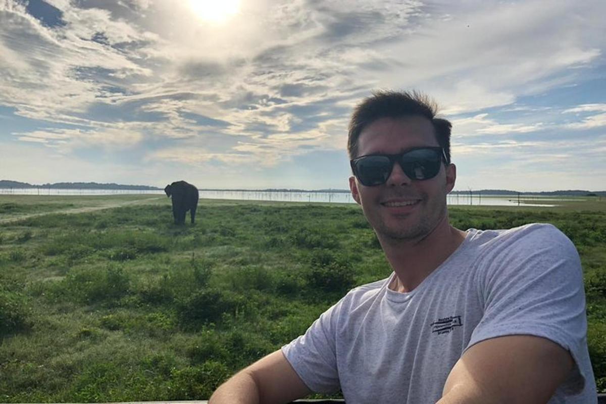 seorang lelaki memakai cermin mata hitam duduk di padang dengan seekor gajah