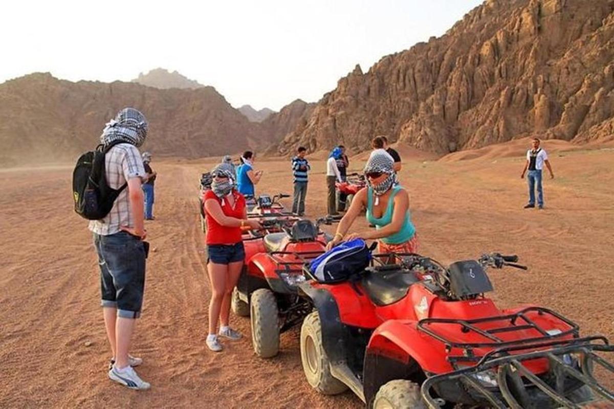 um grupo de pessoas em pé ao redor de quadriciclos no deserto