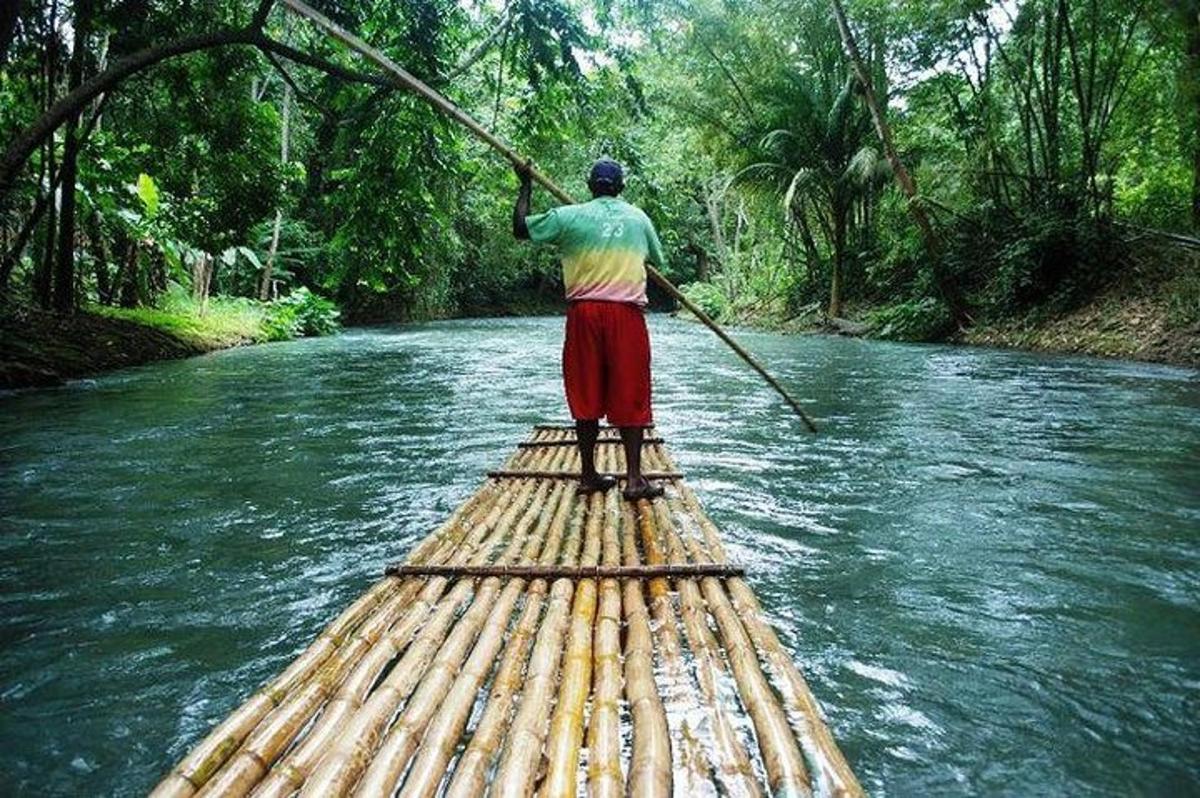 Un hombre está remando en una balsa de bambú en un río.