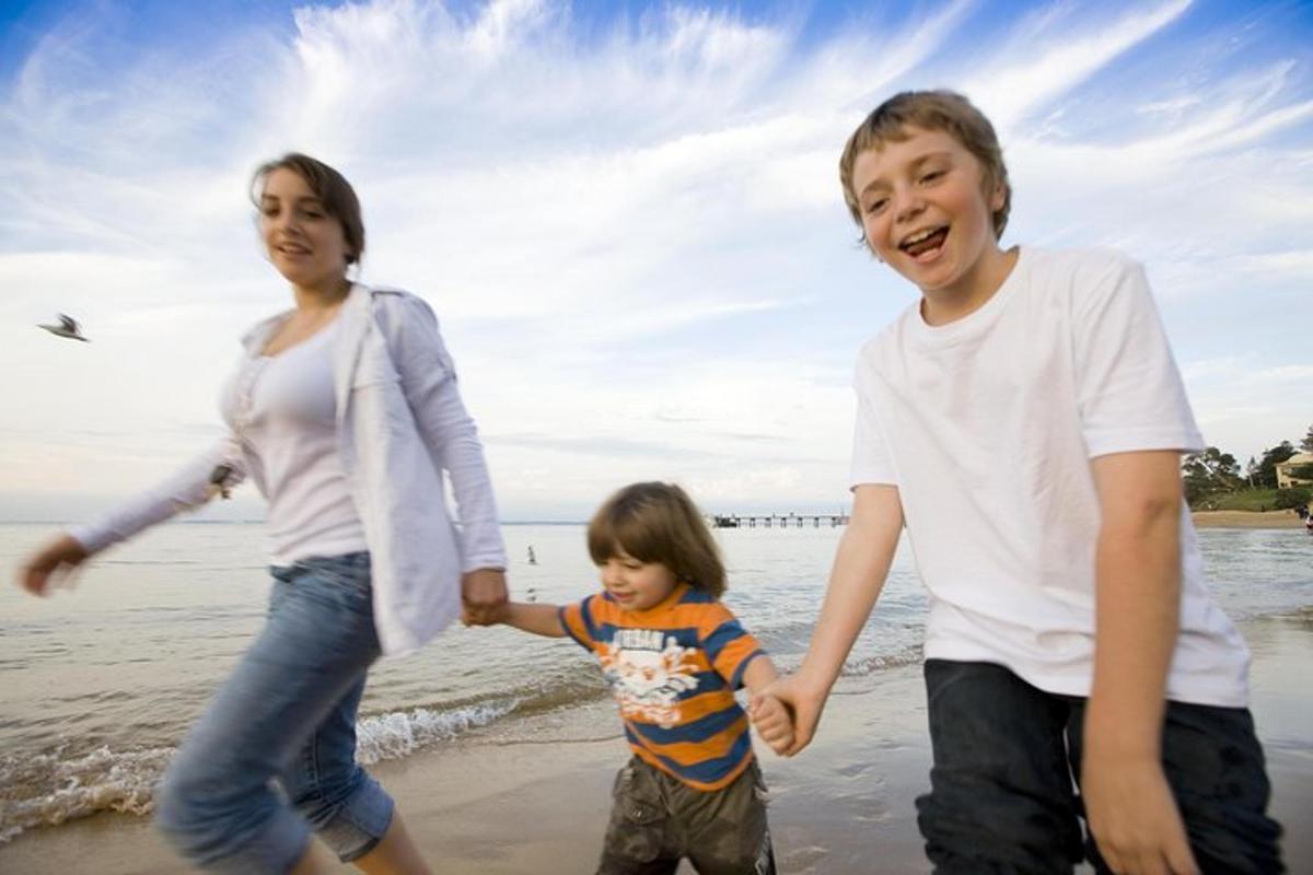 hai người lớn và một đứa trẻ đang chạy trên bãi biển