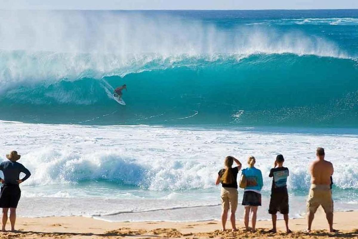 skupina ljudi, ki stojijo na plaži in opazujejo surferja v oceanu