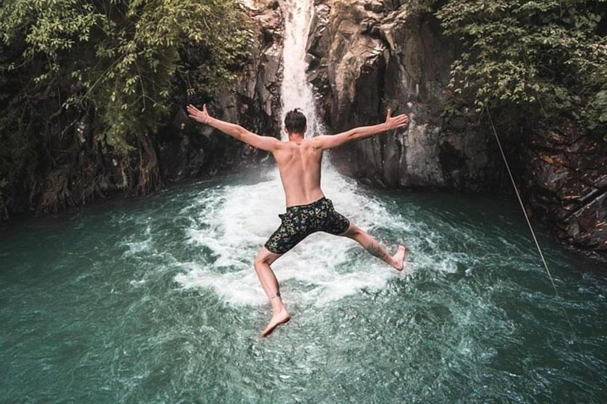 a man jumping into a river in front of a waterfall