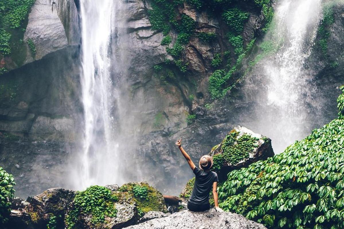 um homem sentado em uma rocha em frente a uma cachoeira