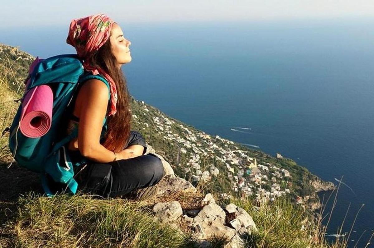 una dona asseguda al cim d'un turó amb una motxilla