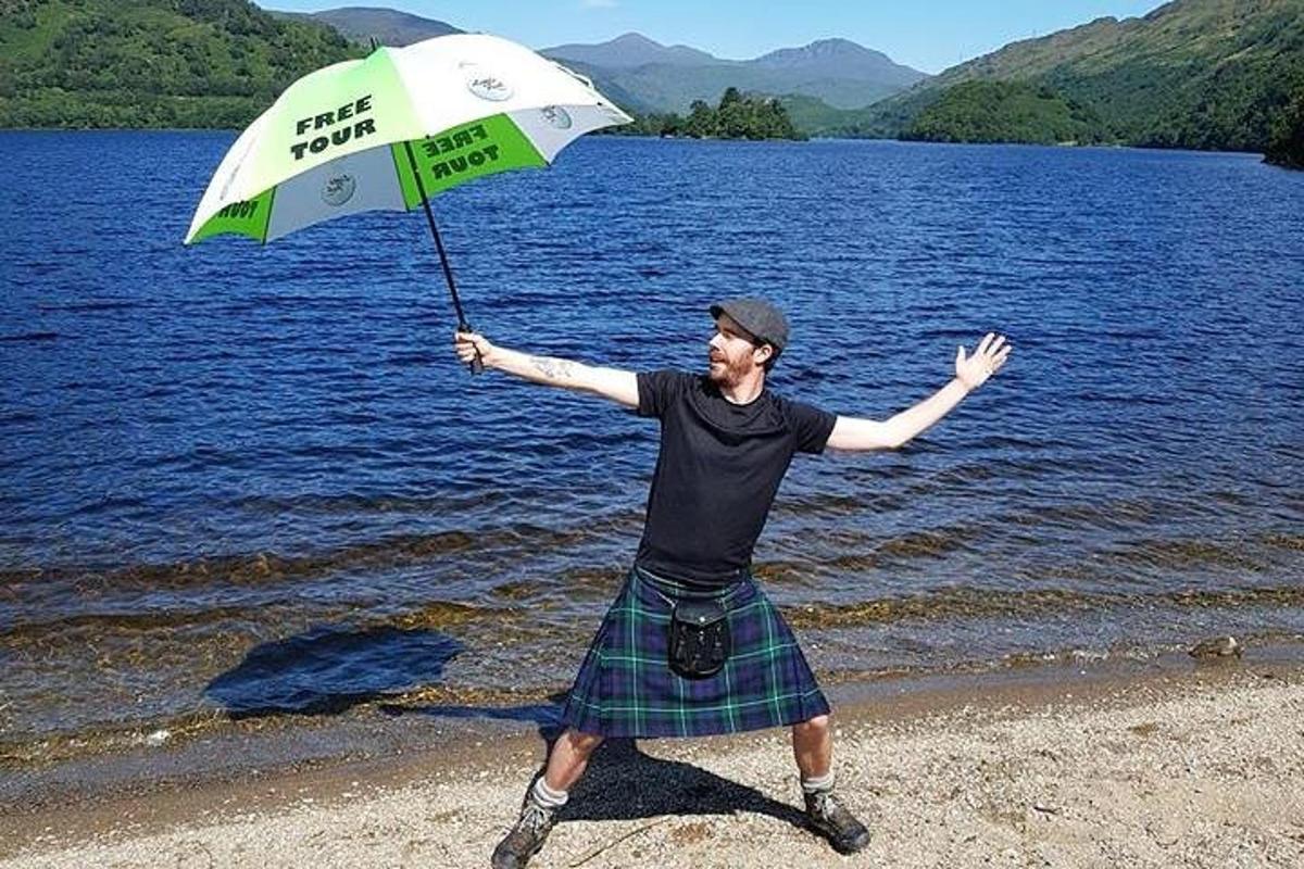 seorang lelaki dalam kilt memegang payung di pantai
